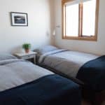 Cozy bedroom with two single beds, white walls, and natural light from a wooden-framed window.