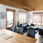 Cozy dining and lounge area with black leather sofas, wooden accents, and ample natural light. Ideal for relaxation and social gatherings.