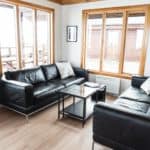 Modern cozy living room with black leather sofas and large wooden framed windows.