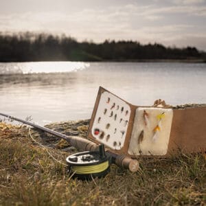 Eiður Kristjánsson signature flies fly box and fly rod on the bank of a lake