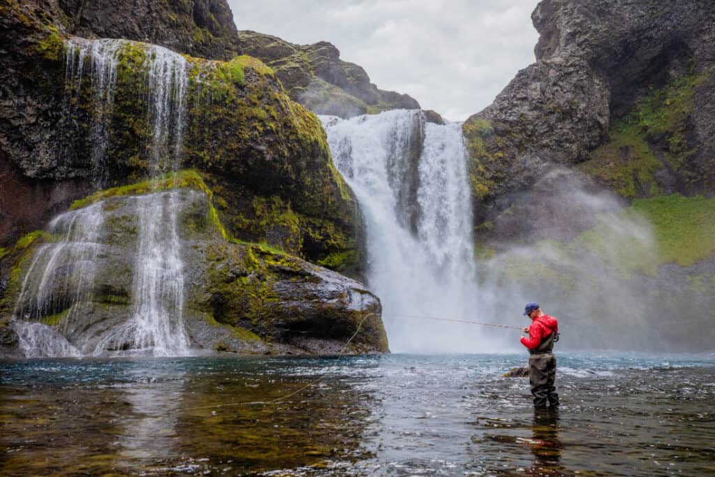 Battle Hill Lodge - Sea Run Brown Trout fly fisherman standing under hagafoss waterfall in geiralandsá river