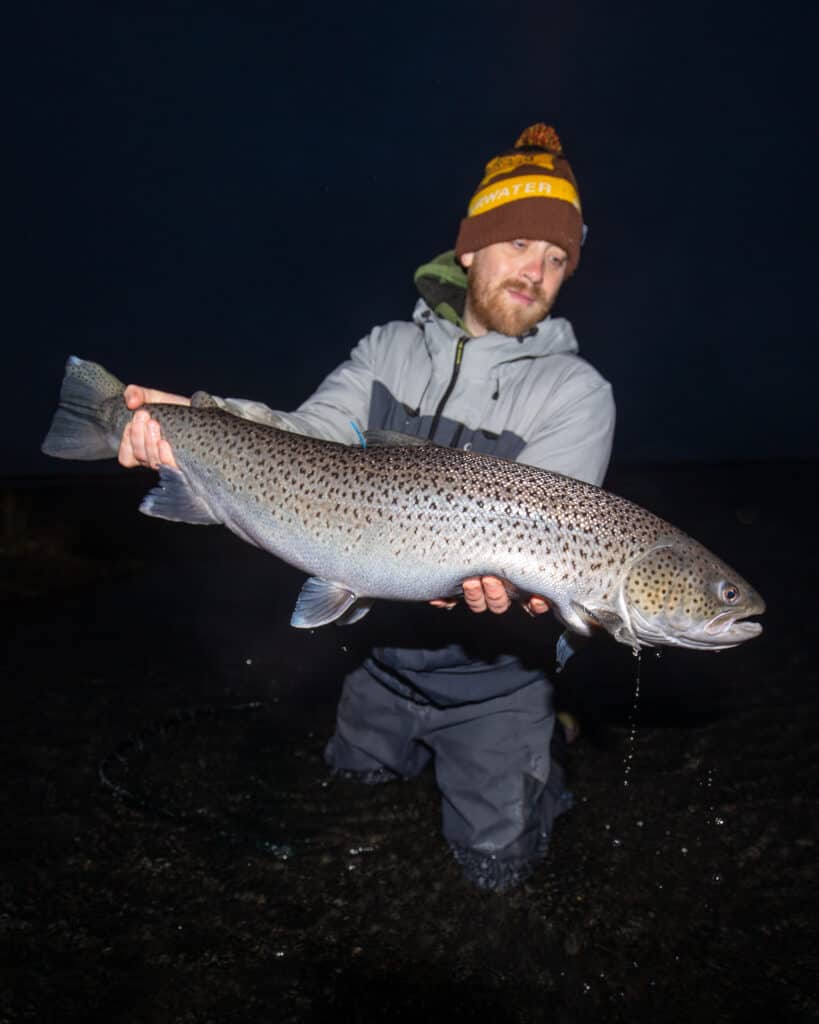 Fisherman holding a large sea trout during night fishing.