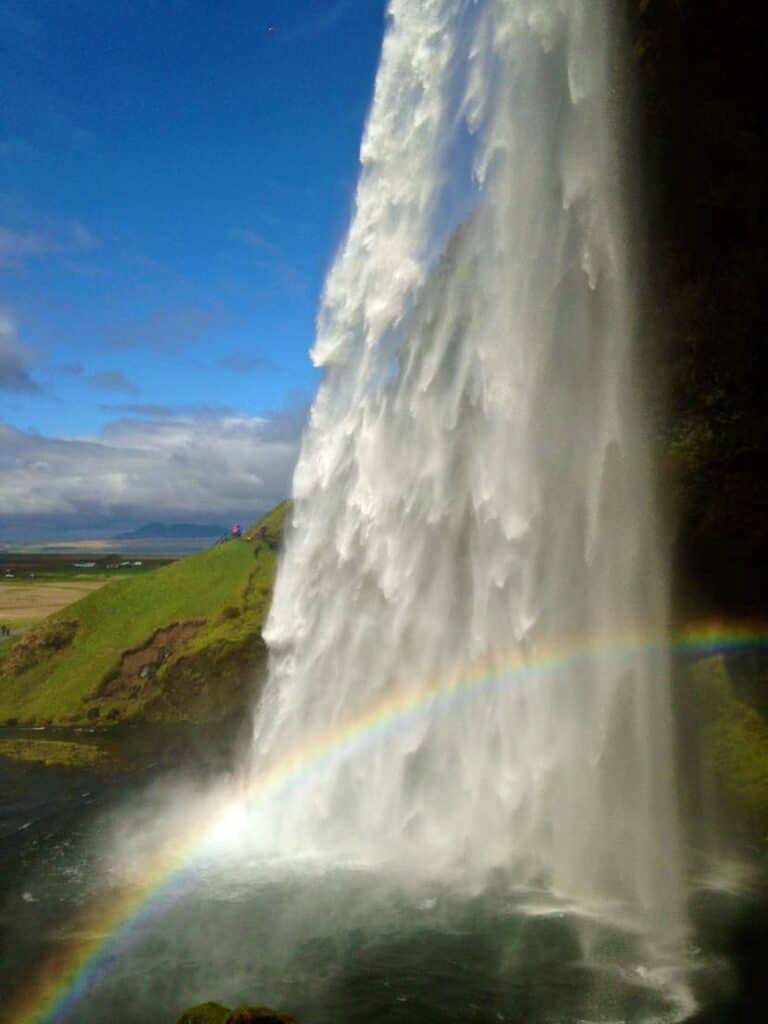 Viking Waterfall in Iceland with rainbow, lush greenery, and blue sky.