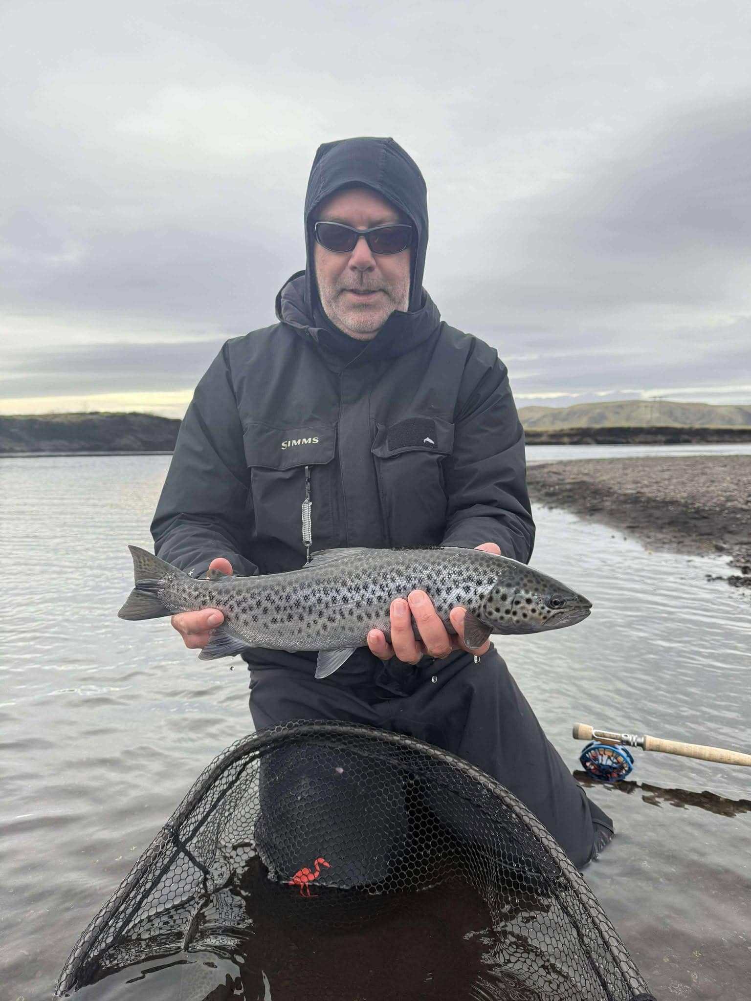 Freshly caught spotted sea trout held by a fisherman in an outdoor river setting.