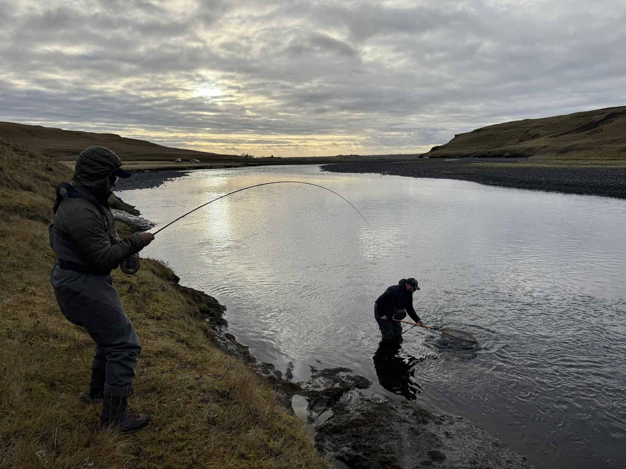 Fishing enthusiasts casting in a scenic river during cloudy weather, engaging in sport fishing.