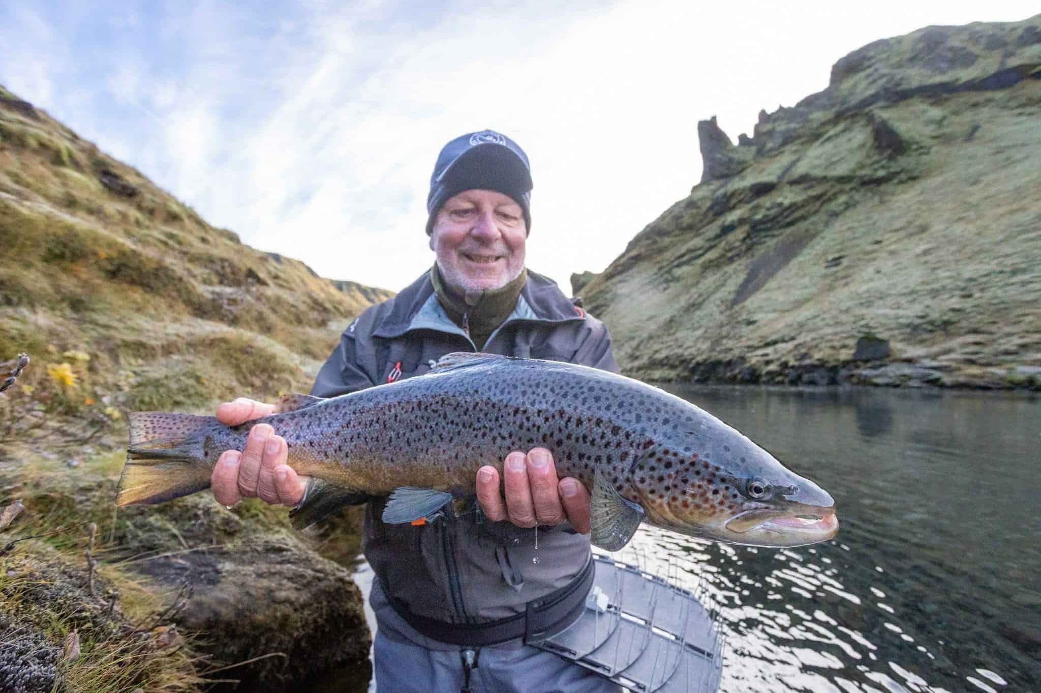 Rainbow trout being held by a fisherman in a scenic river canyon.