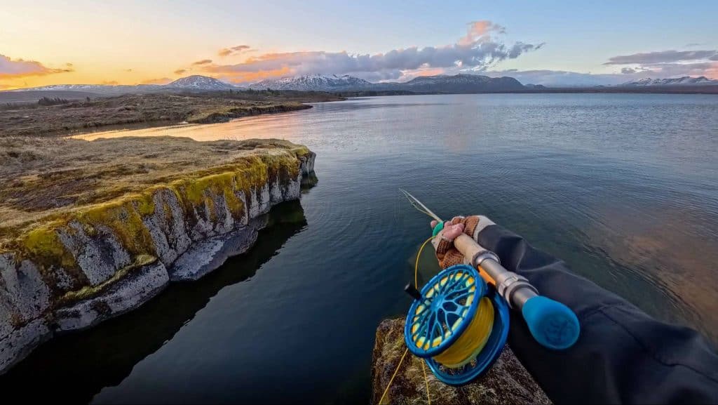 Reed and fishing rod on rocky riverbank with stunning mountain views at sunset in Iceland.