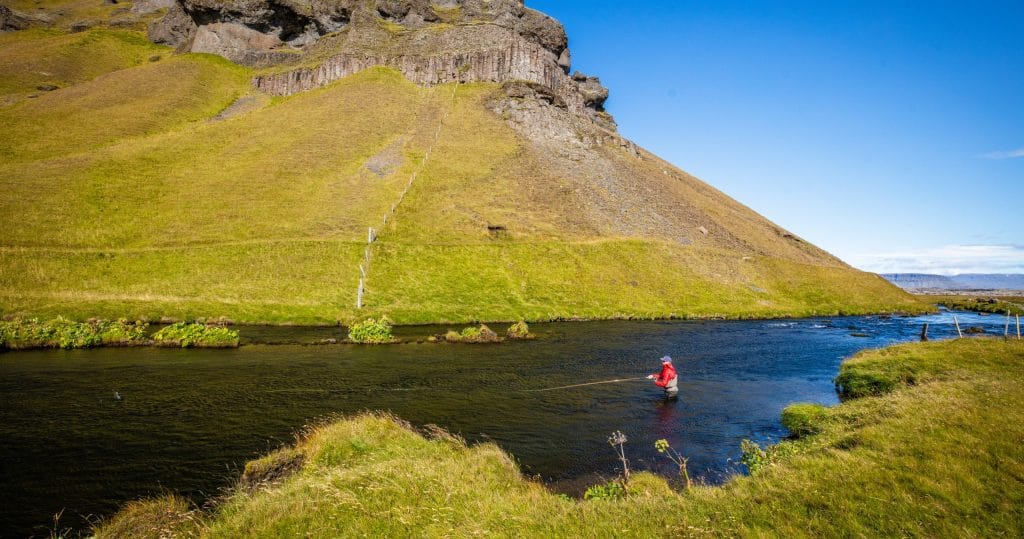 Alpine river fishing scene with Icelandic mountain backdrop in bright daylight.