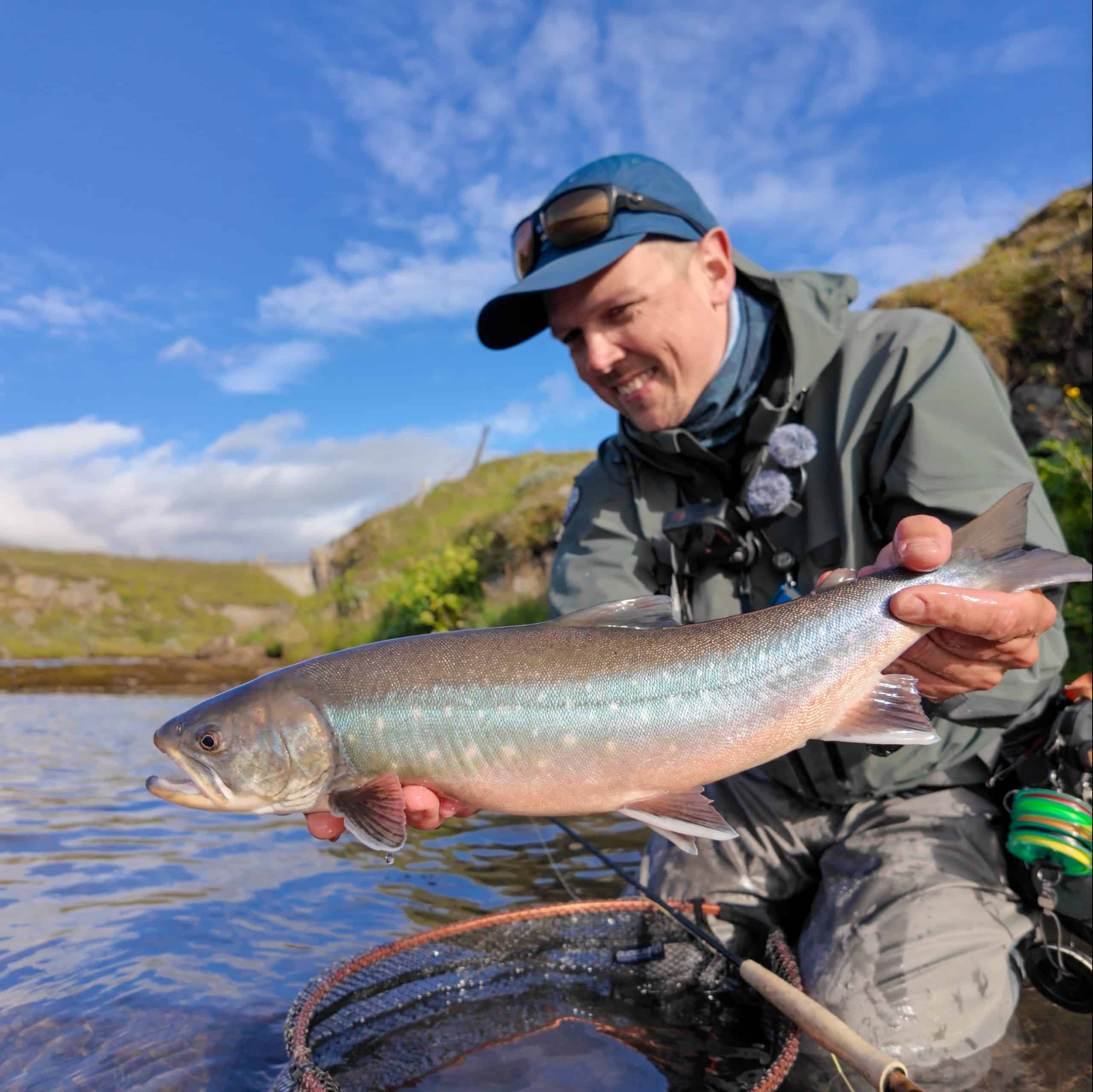 Fisherman holding a freshly caught fish in Icelandic river.
