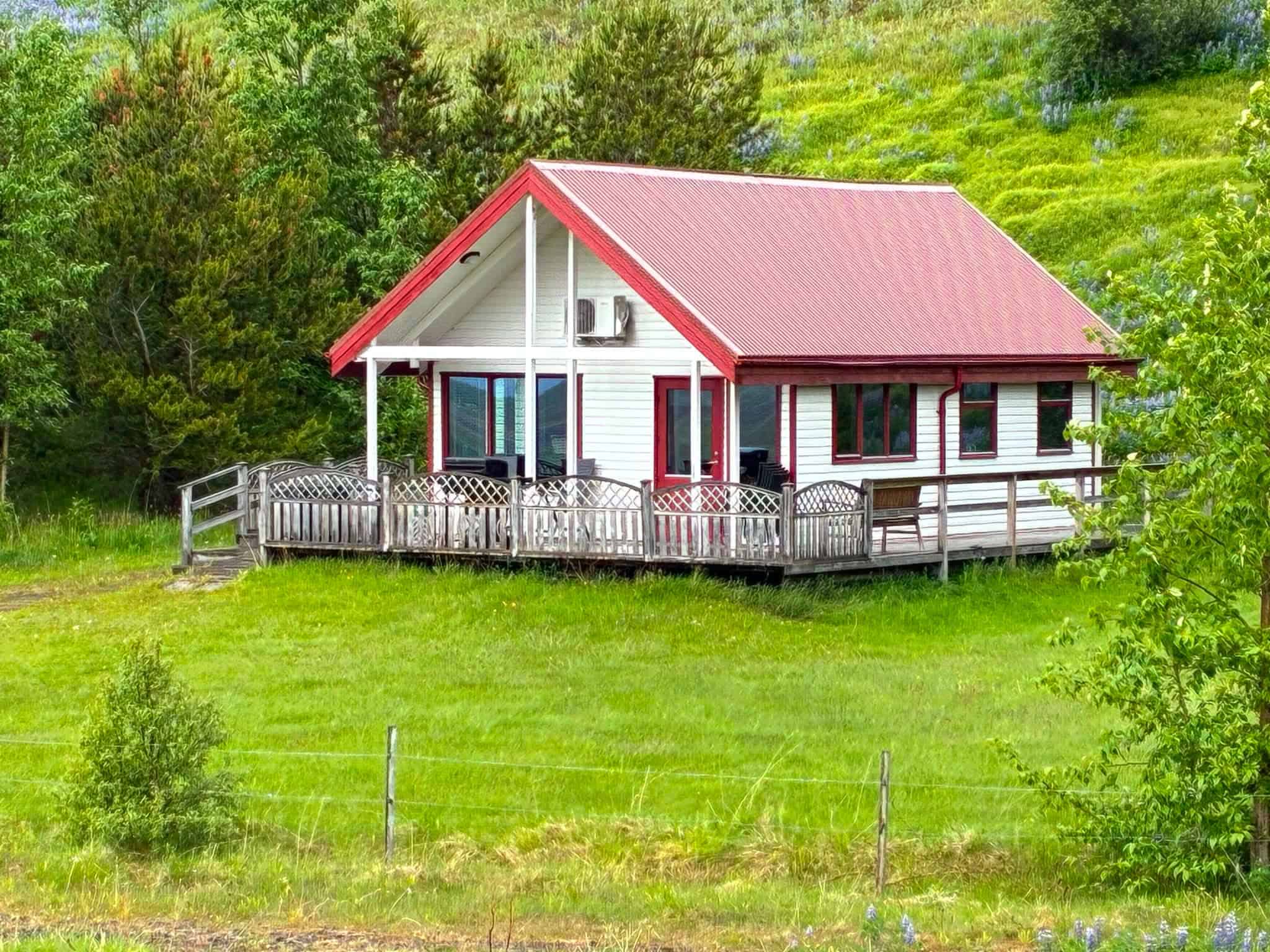 Cozy fishing lodge with red roof in lush green landscape.