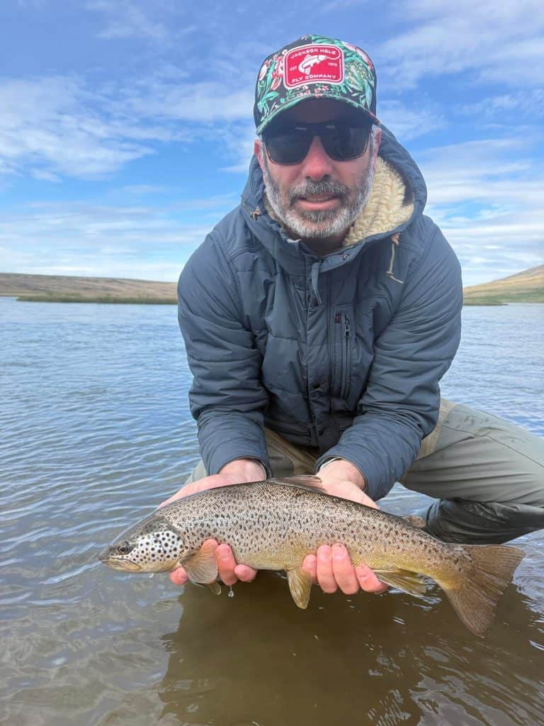 Man holding a fish in a river with blue sky and hills.