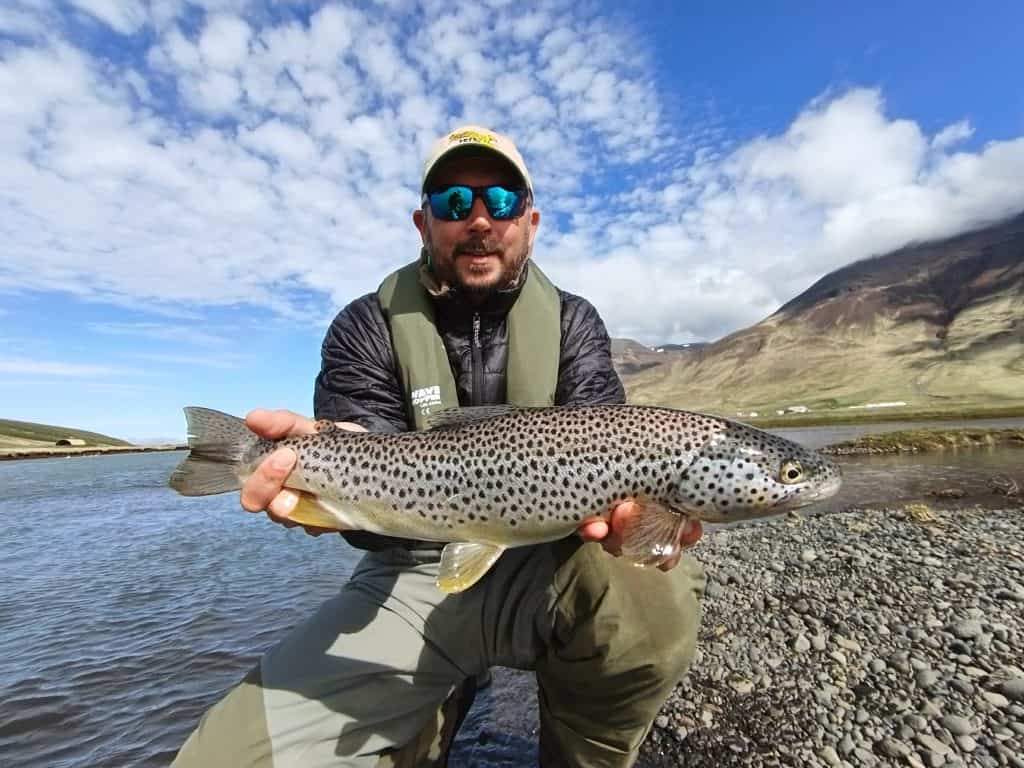 Angler holding a large brown trout by the river.
