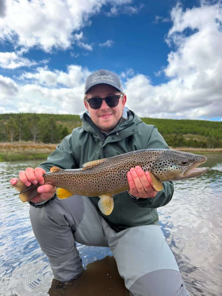 Man holding a large brown trout fish in Icelandic river.
