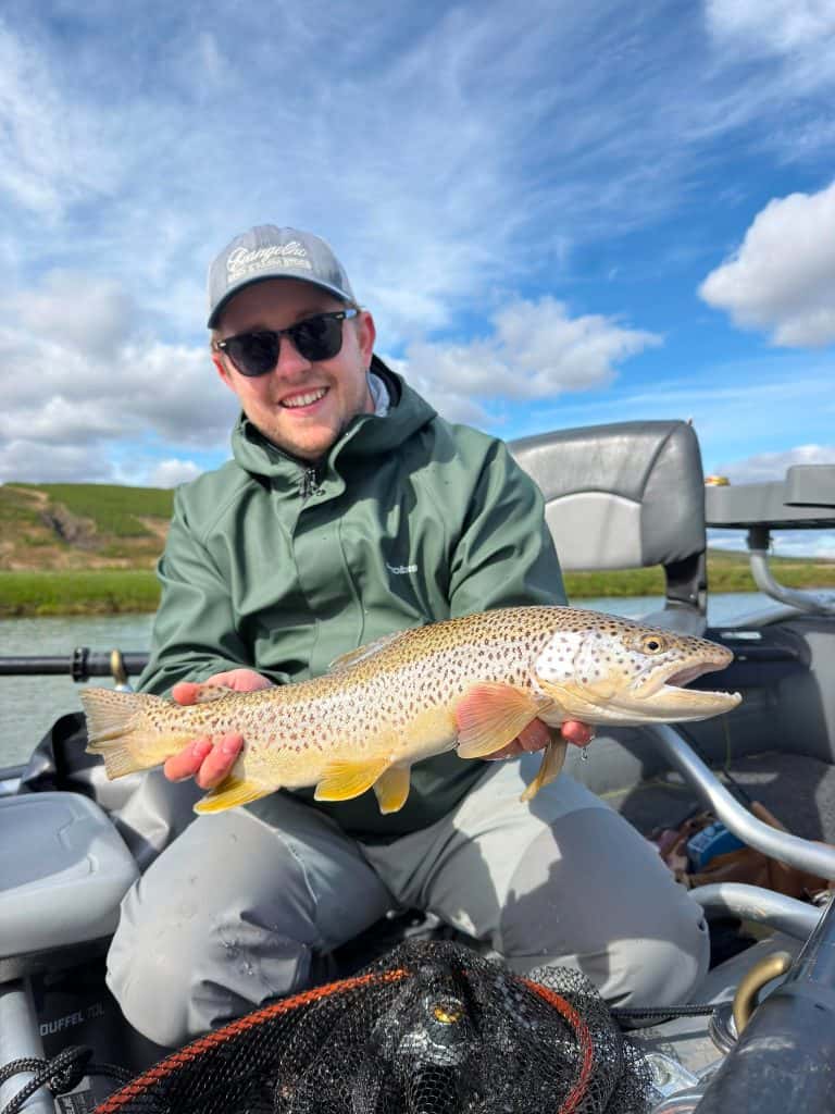 Angler holding a large brown trout on a boat in Icelandic waters.