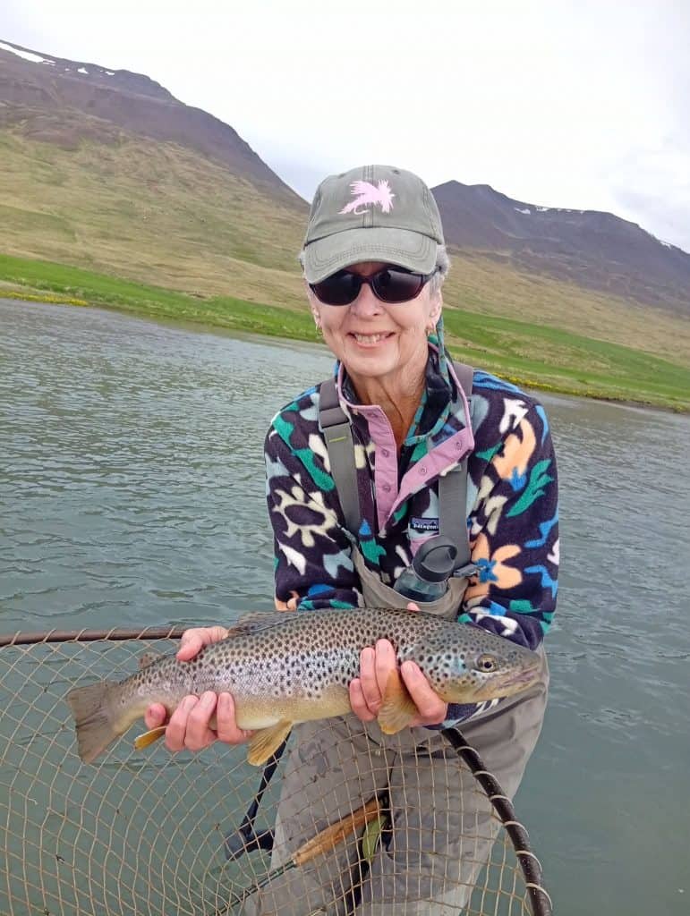 Woman holding a fish in Icelandic river, scenic mountain background.