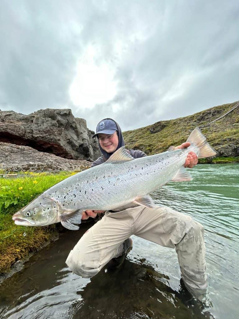 Angler holding a large fish in Icelandic river during cloudy day.