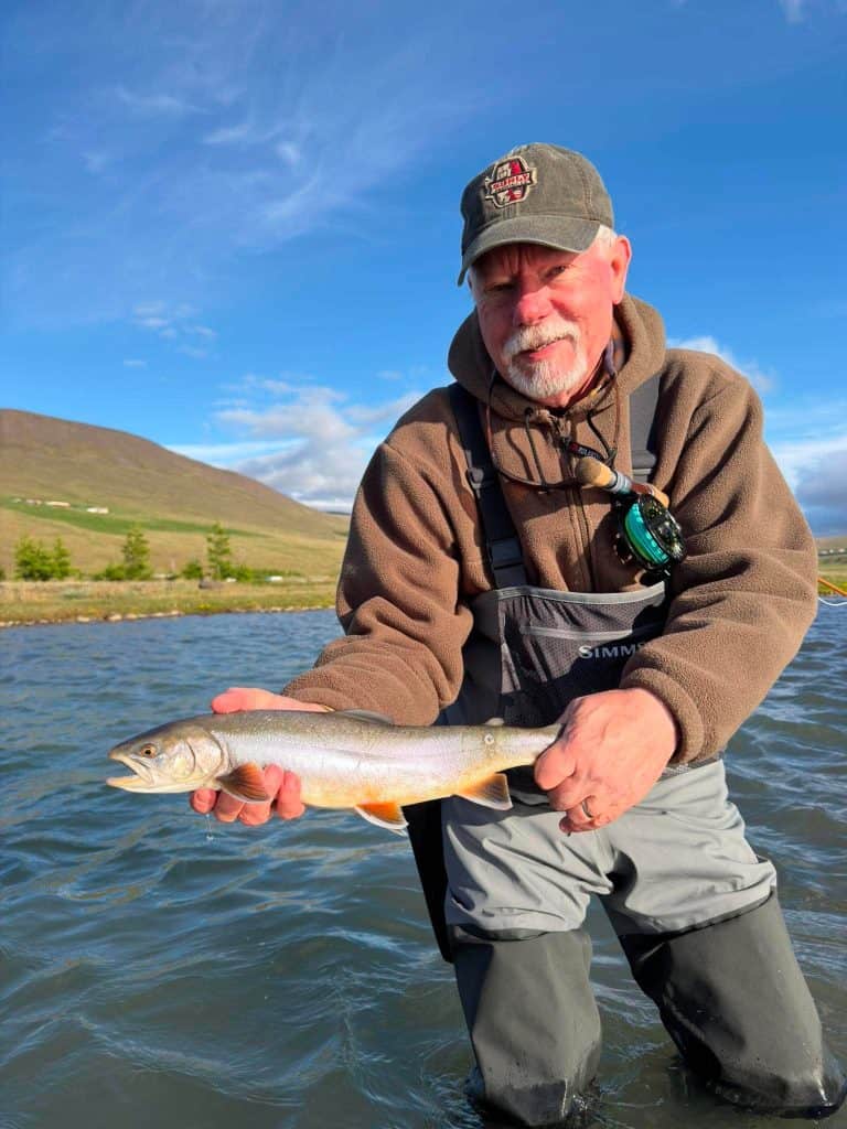 Man holding a fish in a river with scenic landscape background.