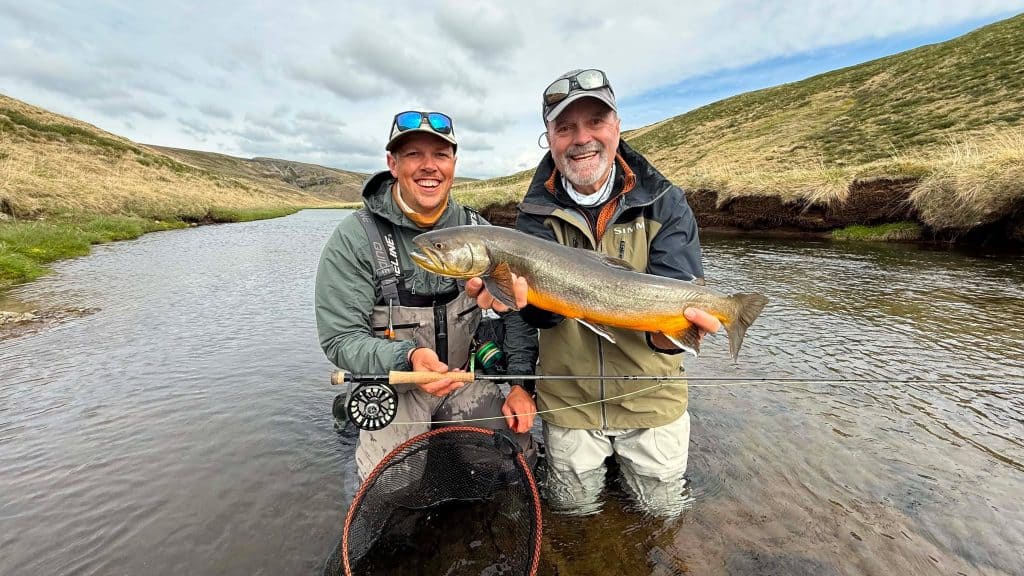 Two anglers holding a sea run brown trout in a river.