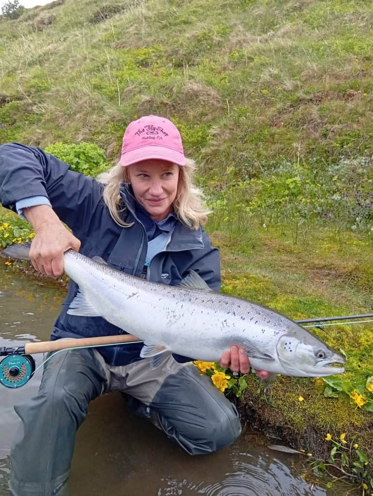Woman holding a large sea run brown trout near water.