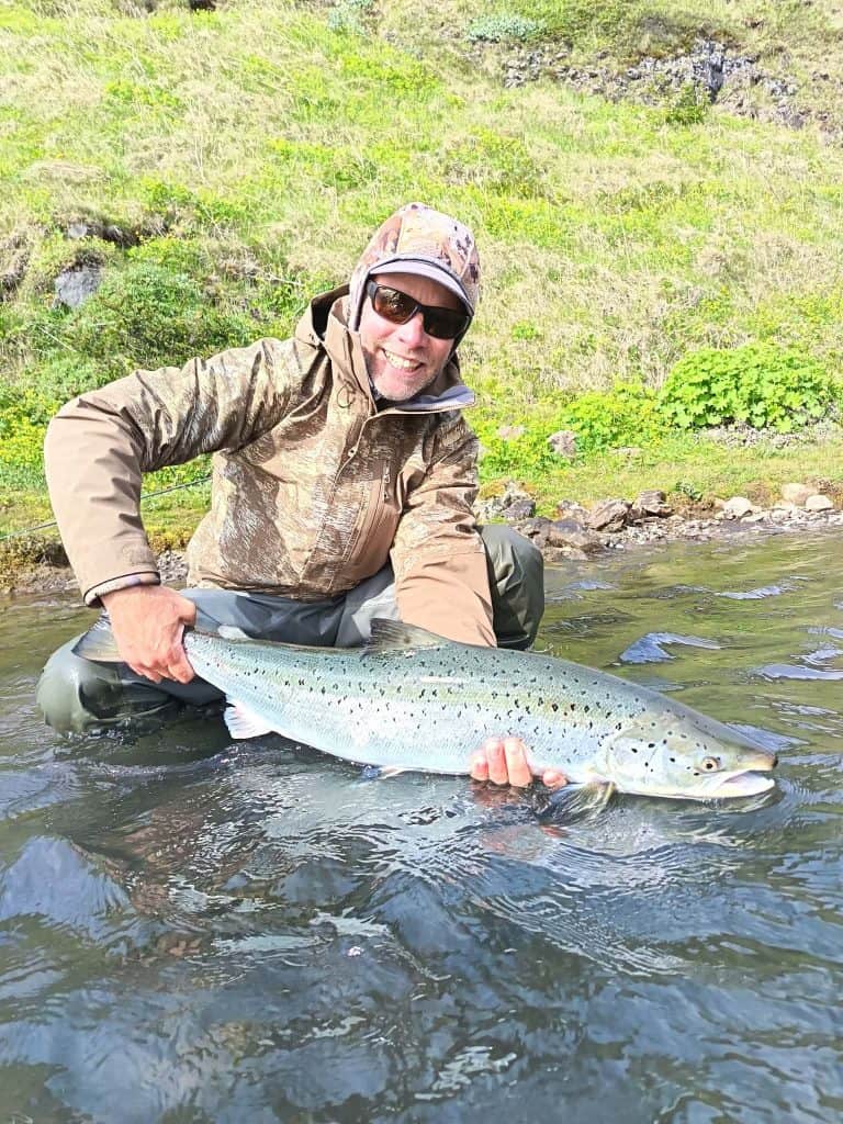 Angler holding a large fish in a river in Iceland.