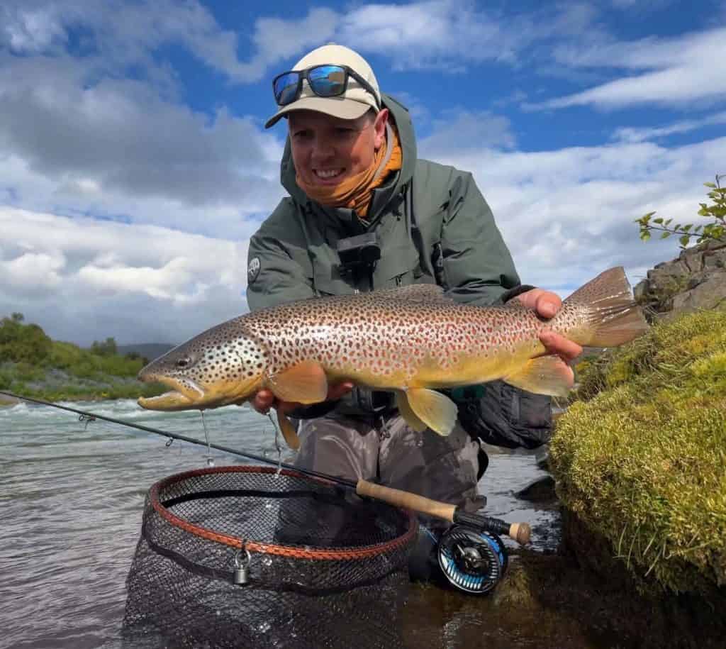Angler holding a large brown trout by a river in Iceland.