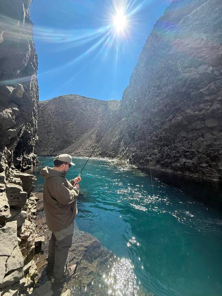 Fisherman casting line in a narrow canyon with clear water and rocky walls.