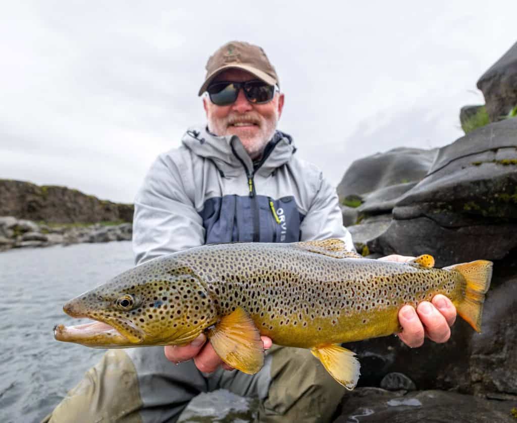 Angler holding a large brown trout by the river.