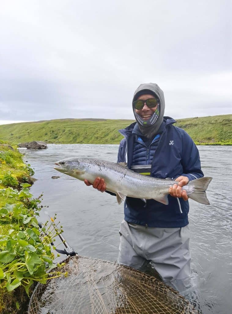 Angler holding a fish in Icelandic river, scenic landscape background.