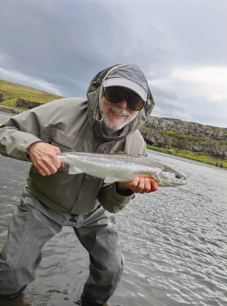 Angler holding a sea run brown trout in a river landscape.