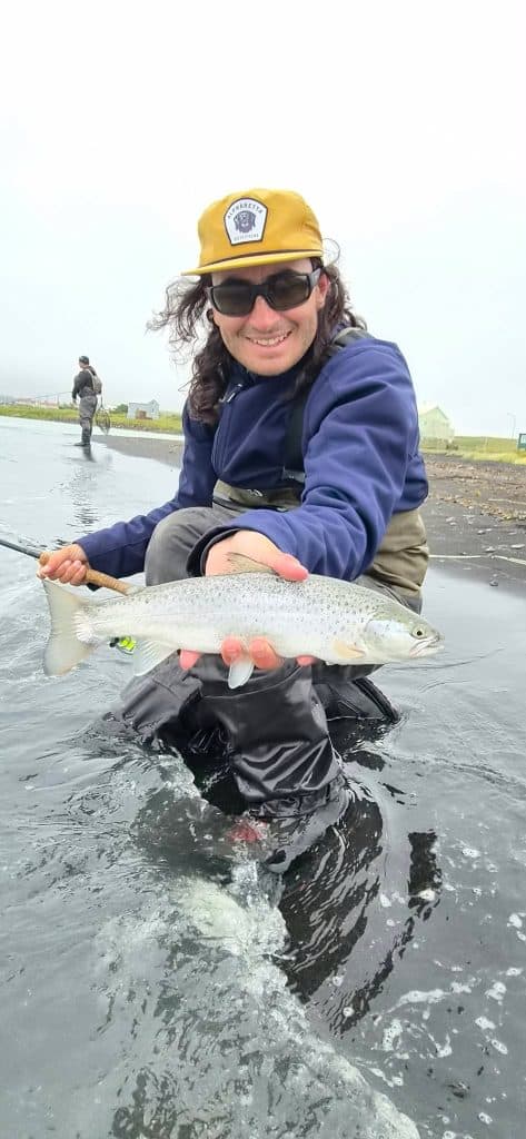 Smiling woman holding a fish in a river during fishing trip.