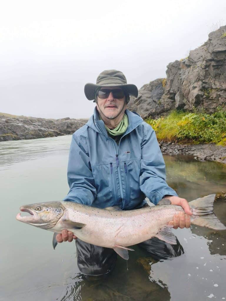 Angler holding a large fish in Icelandic river with rocky cliffs.