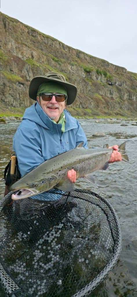Angler holding a large fish in a river with cliffs in the background.