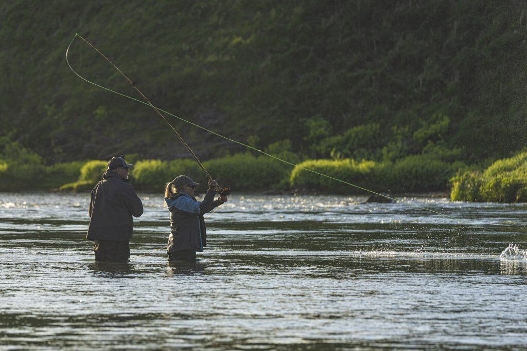 Two anglers fishing in a river with lush green surroundings.