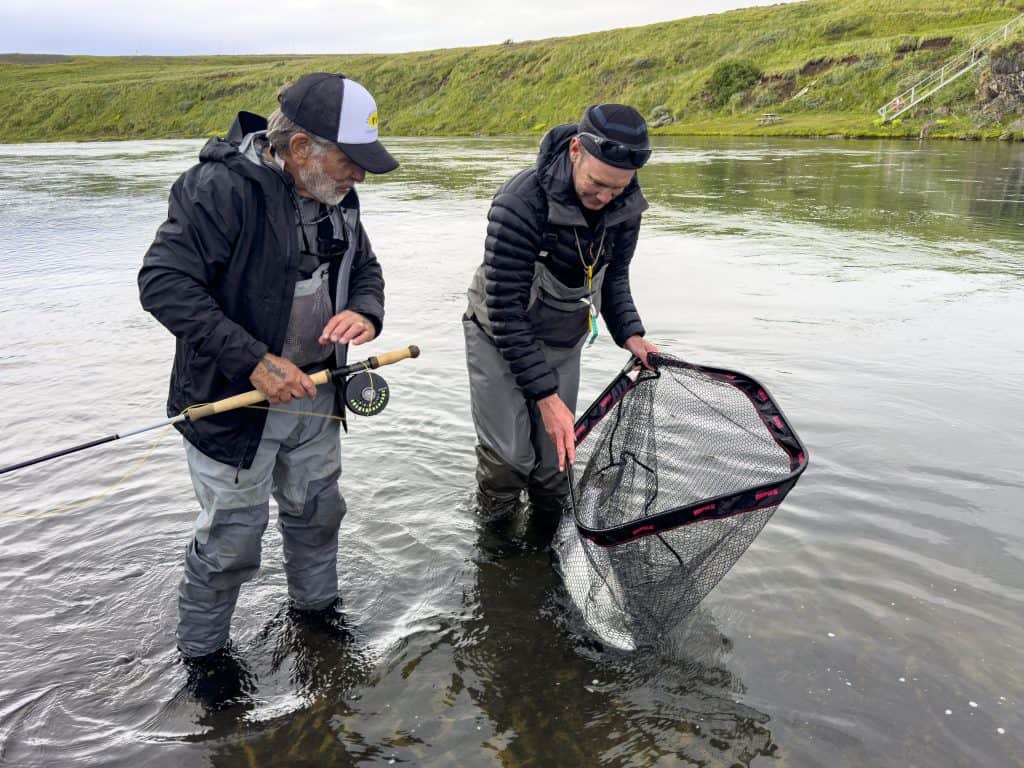 Two anglers fishing in a river with a fishing net and gear.