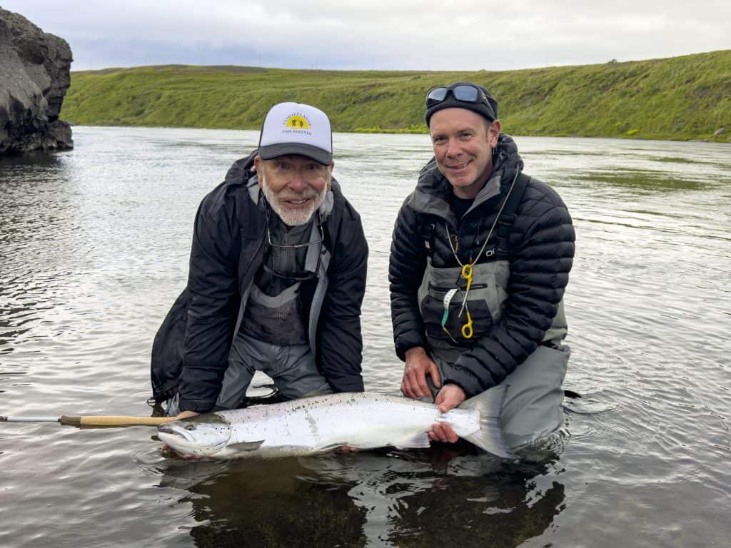 Two men holding a fish in a river in Iceland.