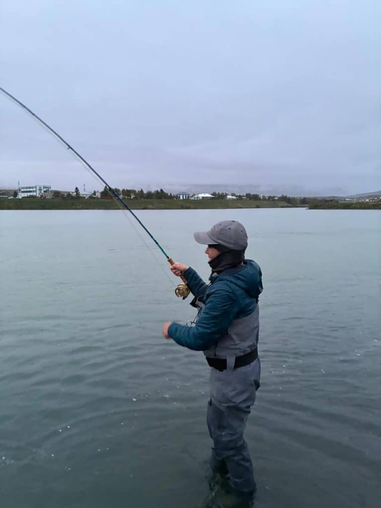 Angler fishing in a calm Icelandic lake with overcast sky.