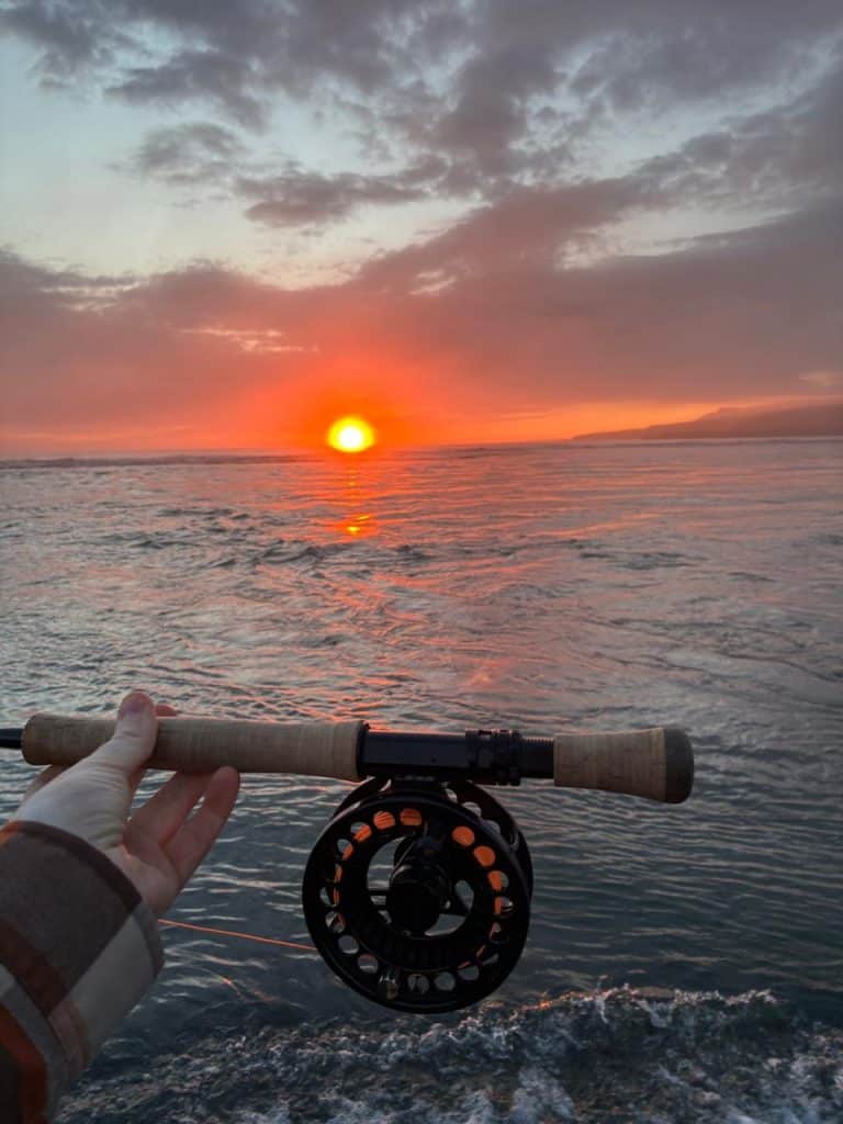 Fishing rod pointed at sunset over water during evening.
