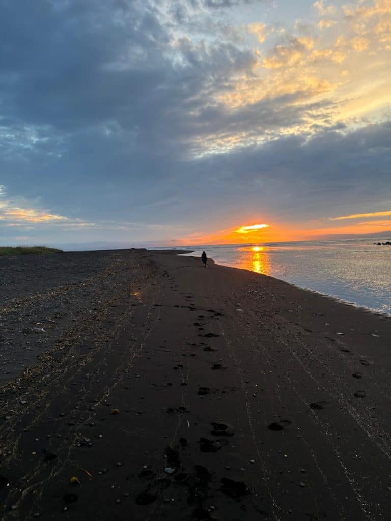 Scenic sunset over a beach with footprints and a person walking.