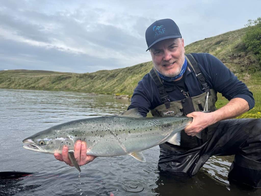 Man holding a large sea run brown trout in a river.