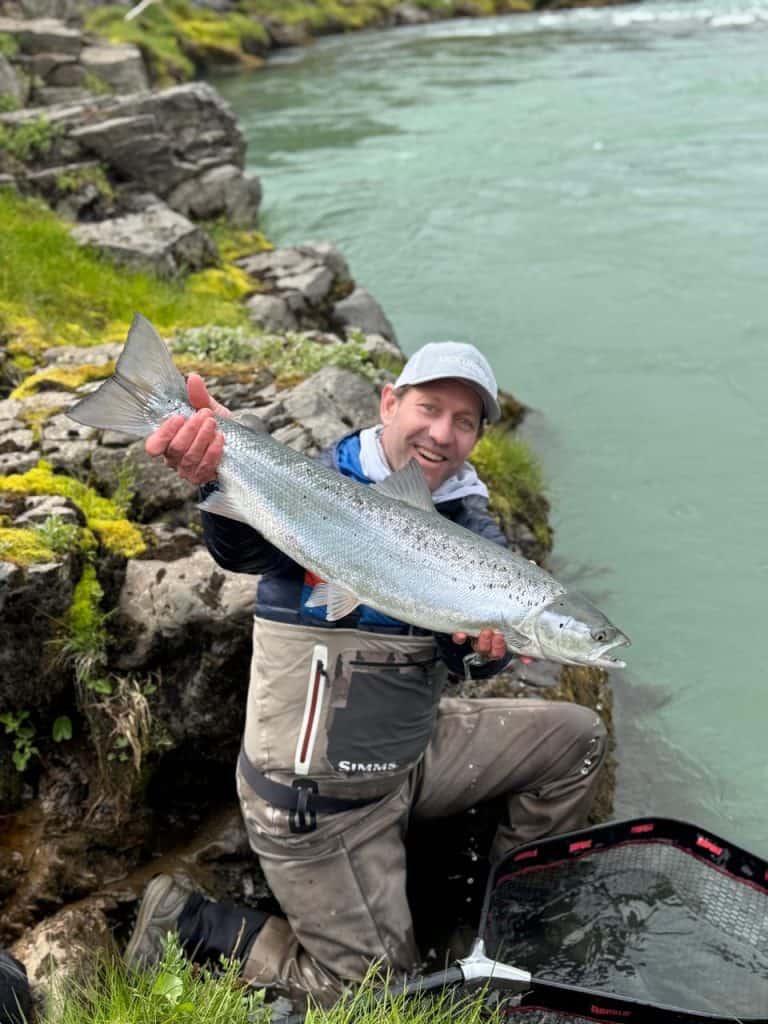 Fisherman holding a large fish by the riverbank in Iceland.