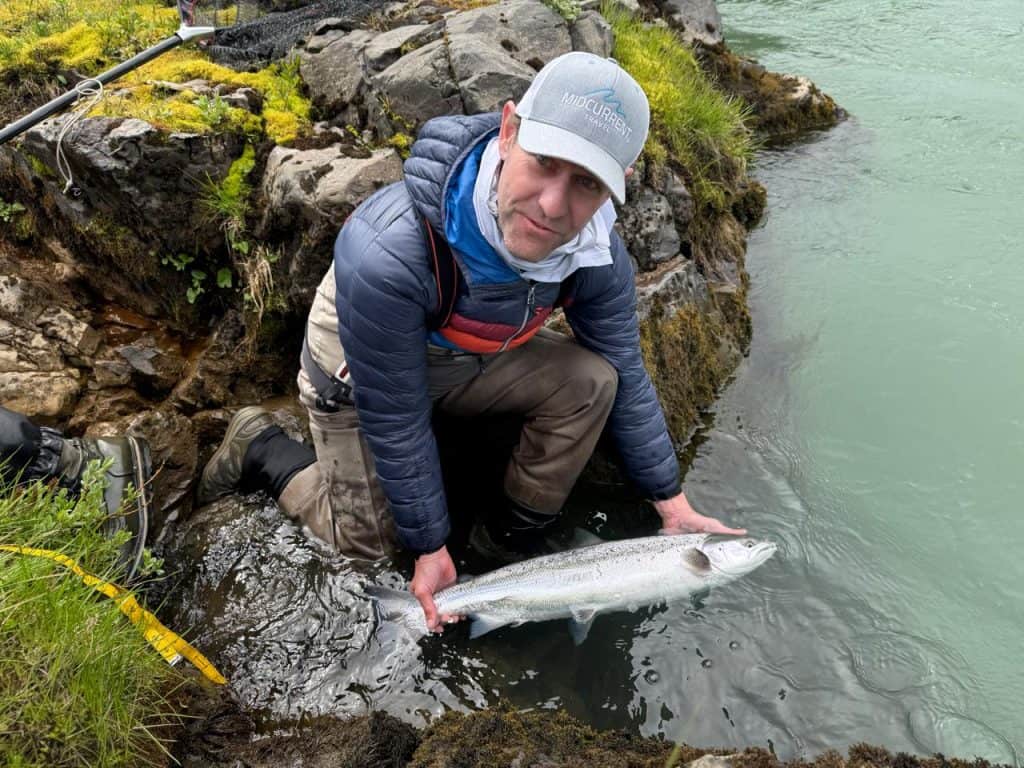 Angler holding a fish near rocky riverbank in Iceland.