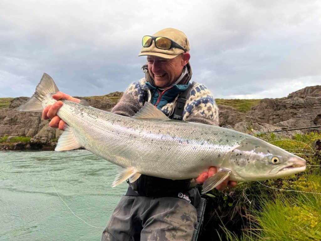 Angler holding a large sea run brown trout near rocky shoreline.