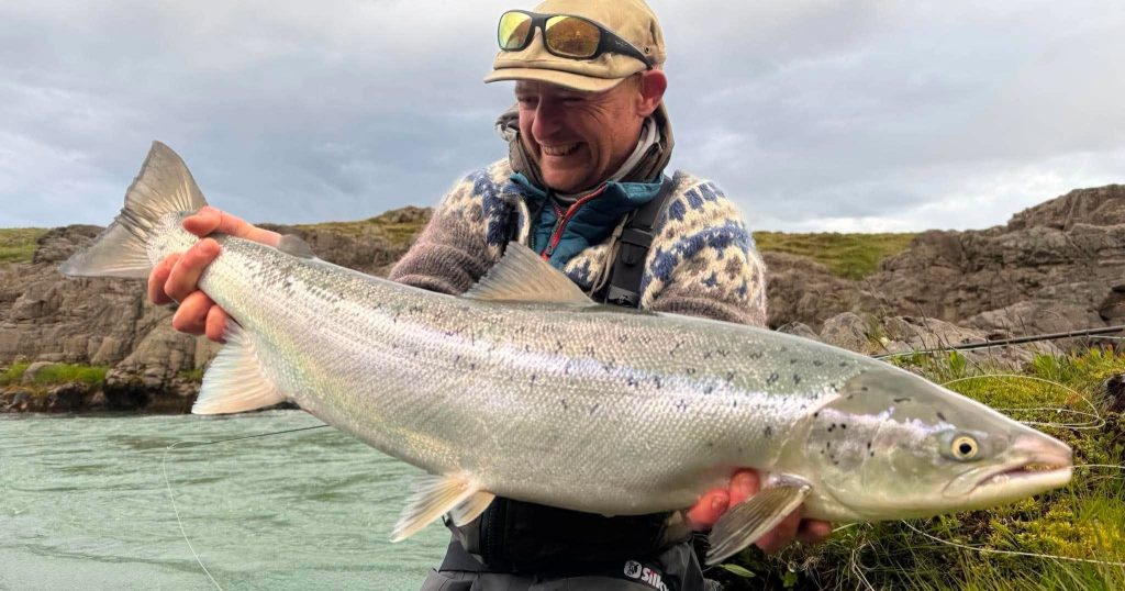 Angler holding a large sea run brown trout near rocky shoreline.