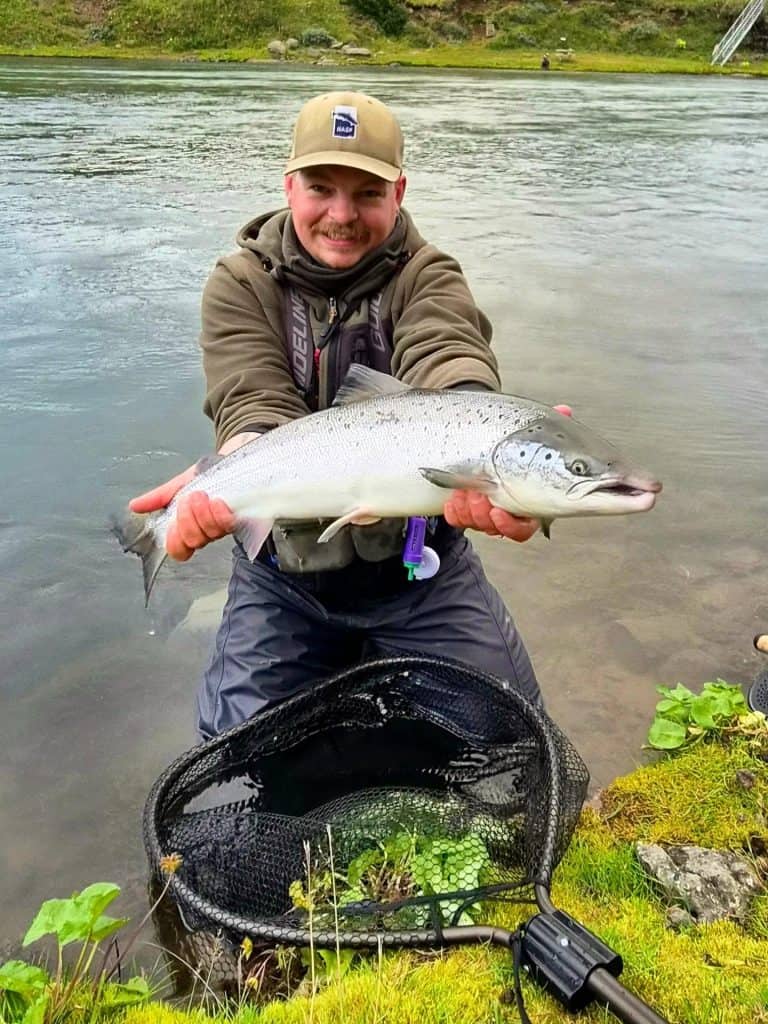 Fisherman holding a sizable fish near a riverbank.