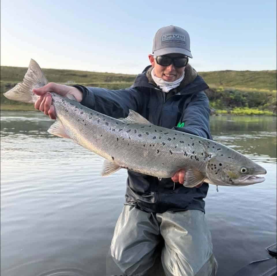 Person holding a large fish near a river with green hills in the background.