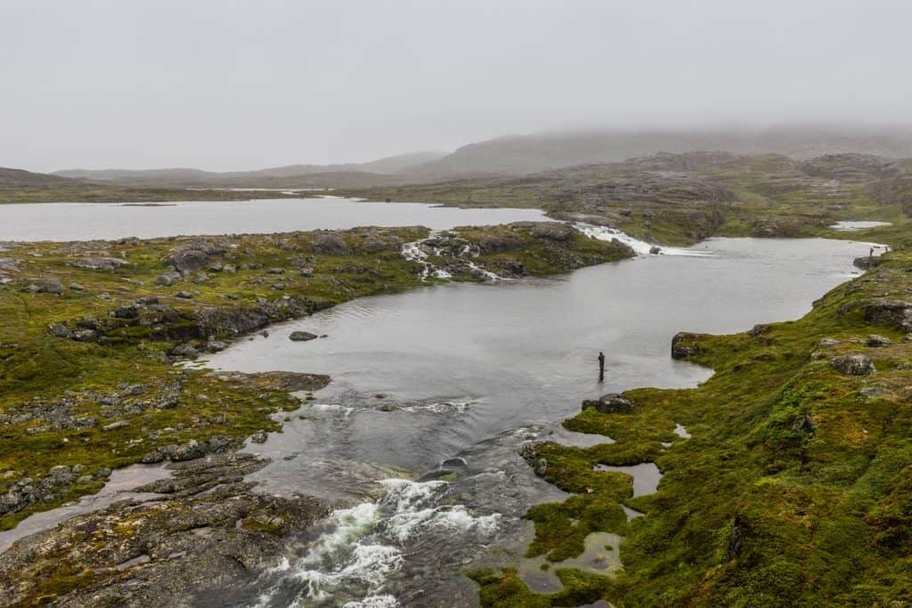 Misty river scene with mossy banks and a fly fisherman in the distance.