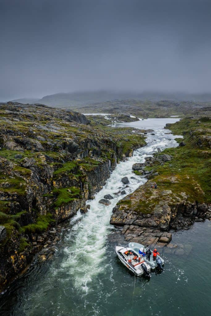 Two anglers fly-fishing from a boat in a narrow river canyon in Greenland.