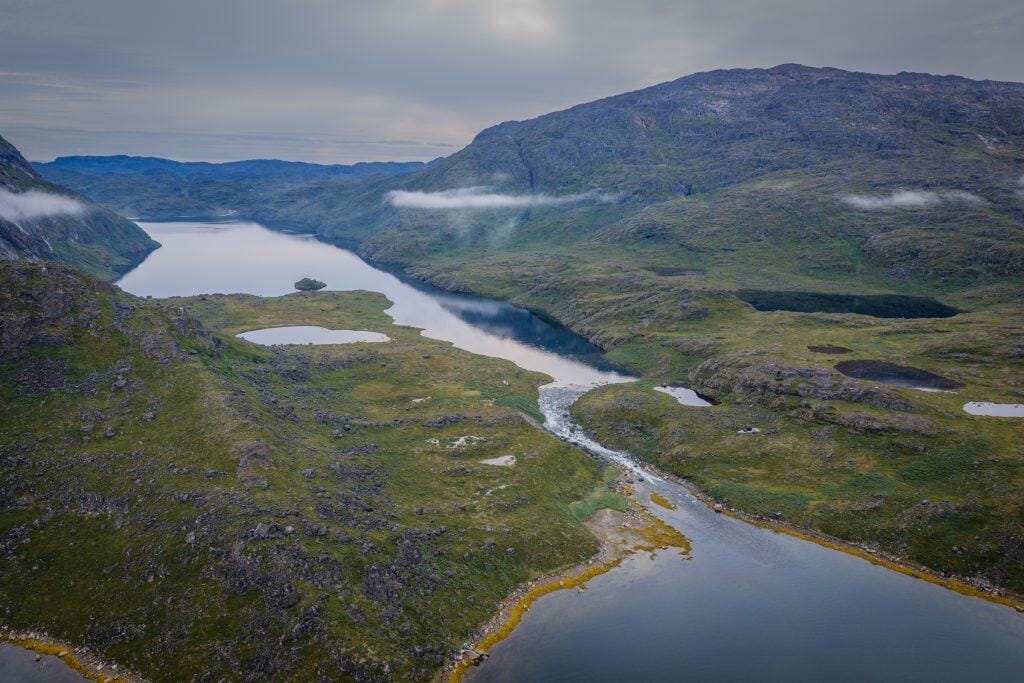 Aerial view of a winding river through lush green mountains in Greenland.