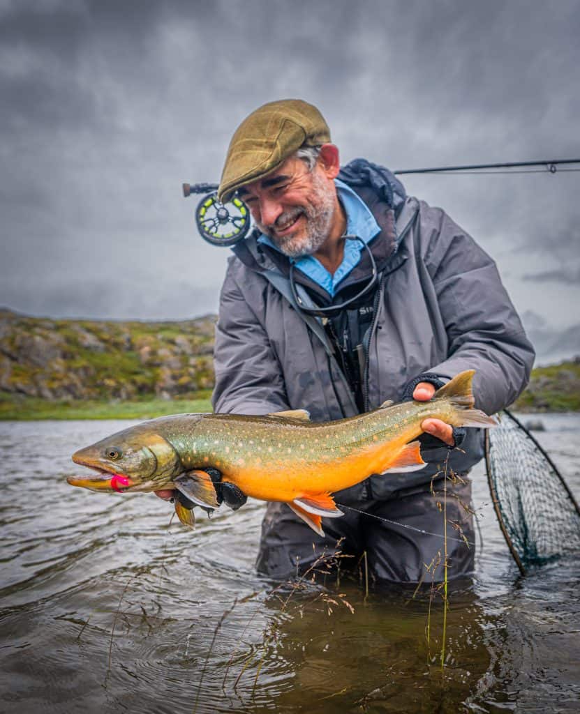 Angler holding a freshly caught Arctic Char in a river.