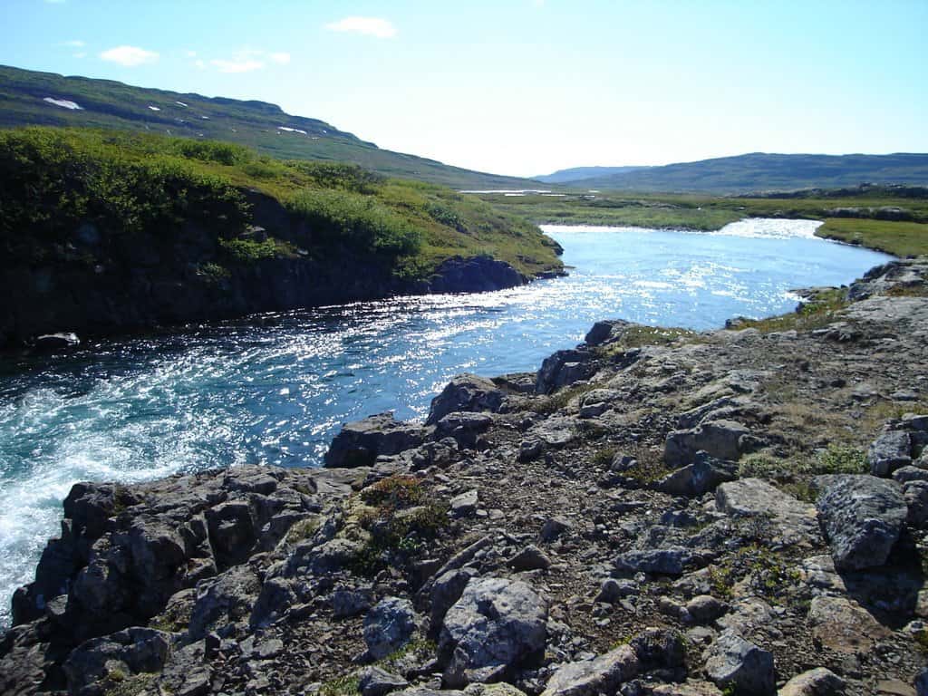 Scenic view of Bjarnarfjarðará river with rocks and lush greenery.